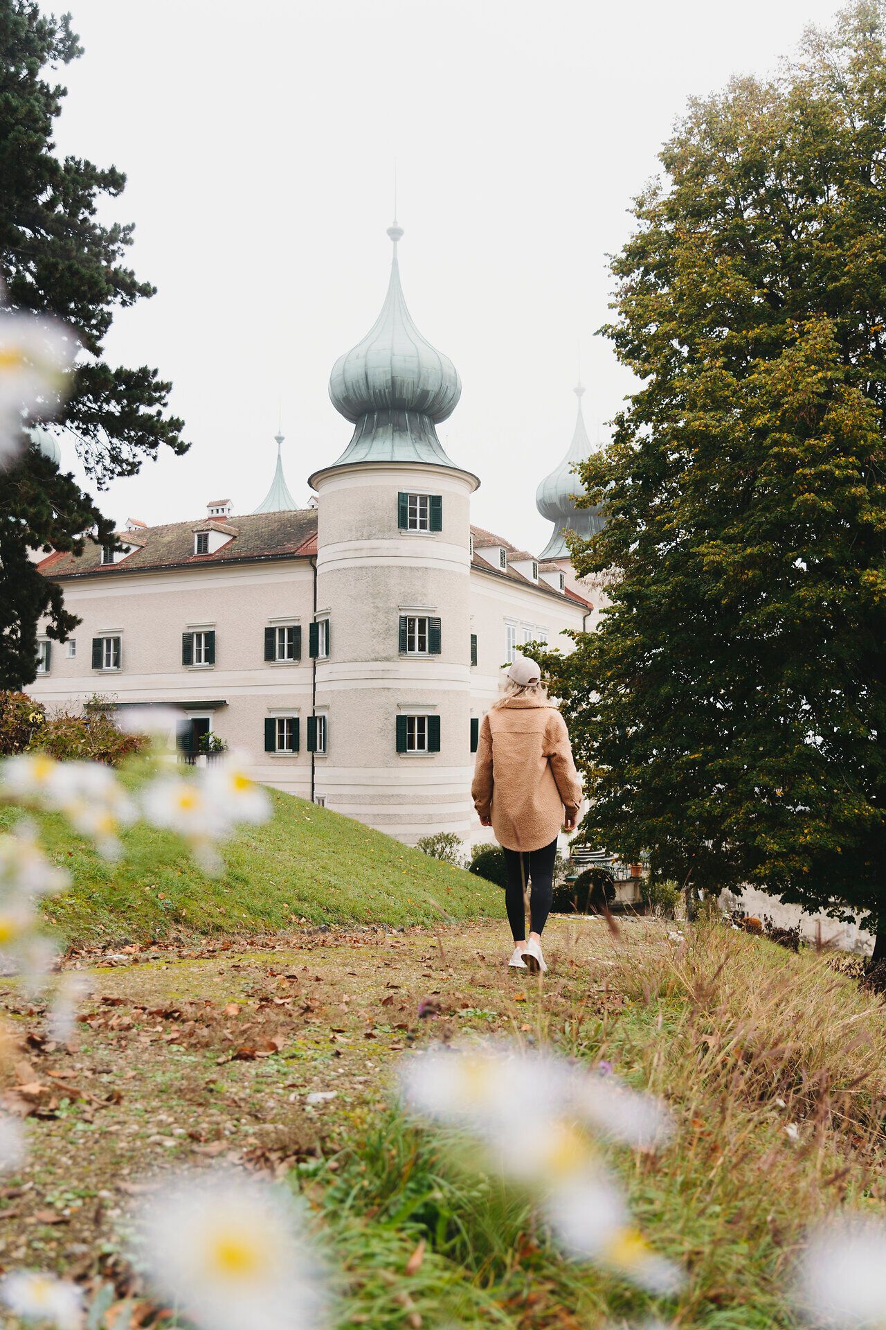 In der sanften Herbstlandschaft des südlichen Waldviertels schlendert eine Person auf einem malerischen Pfad, umgeben von bunten Blättern und der majestätischen Kulisse des Schlosses. Die harmonische Verbindung von Natur und Architektur schafft eine einladende Atmosphäre, die zum Verweilen einlädt.