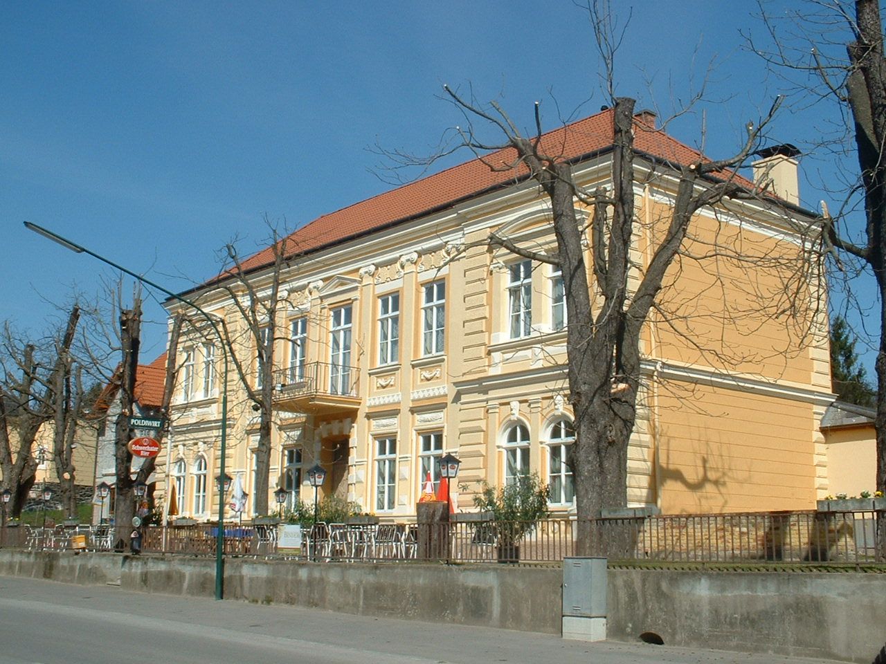 Gelbes Gebäude mit rotem Dach und kahlen Bäumen davor.
