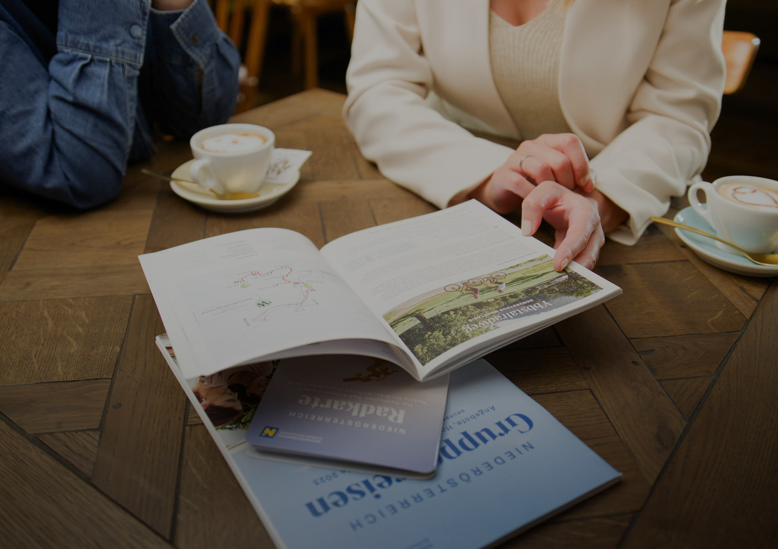 Prospektmaterial liegt am Tisch und wird bei einer Tasse Kaffee hergezeigt. 