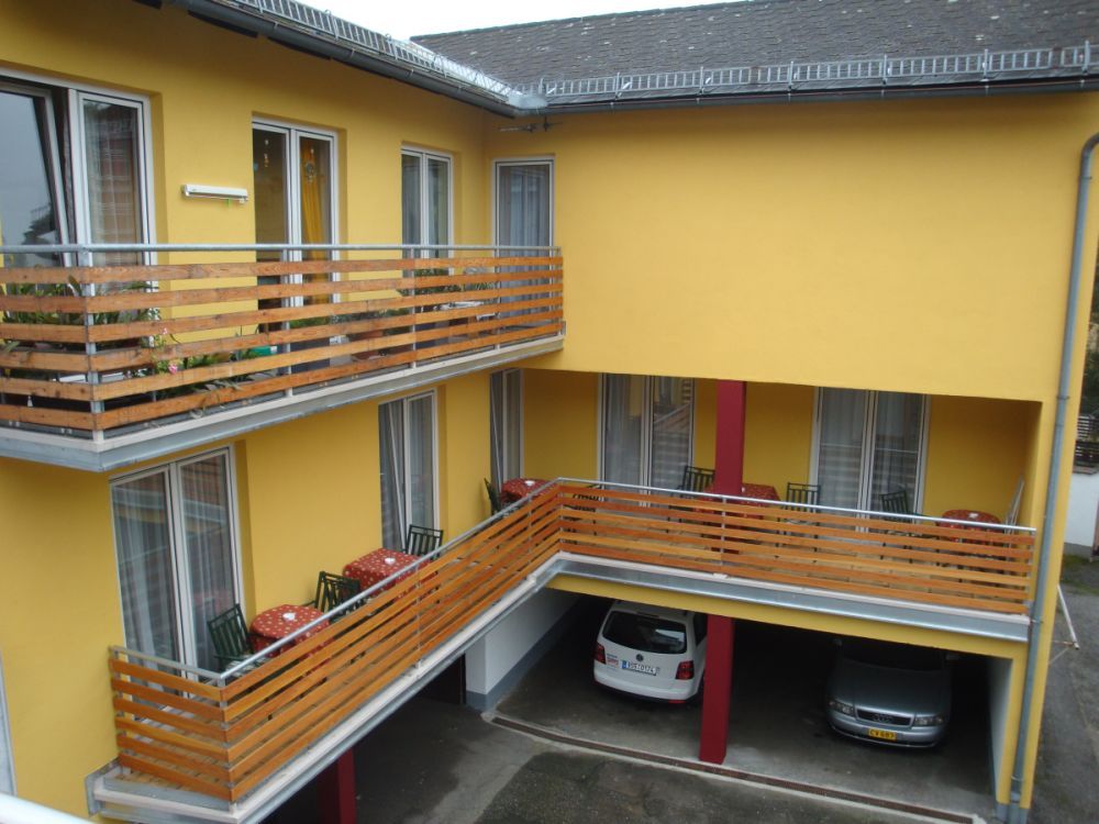 Gelbes Gebäude mit Balkonen und geparkten Autos darunter.