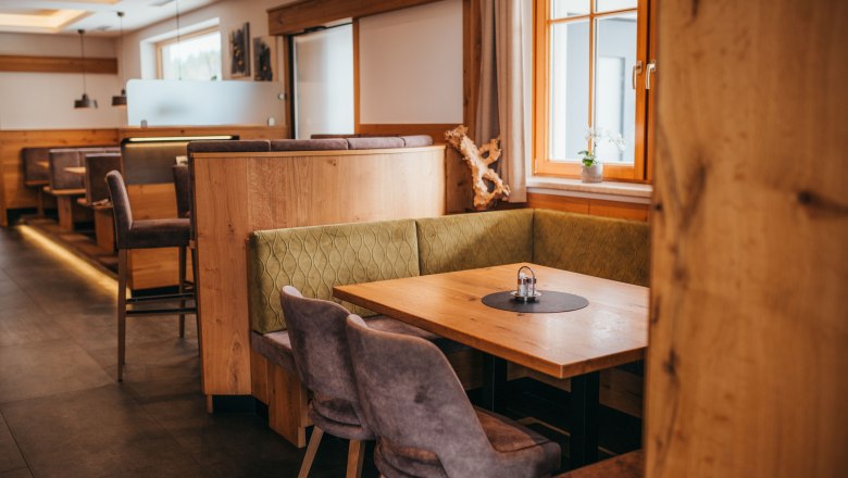 Gemütliche Gaststube mit Holzmöbeln und gepolsterten Sitzbänken, Fenster mit Vorhängen, Tisch mit Salz- und Pfefferstreuer.
