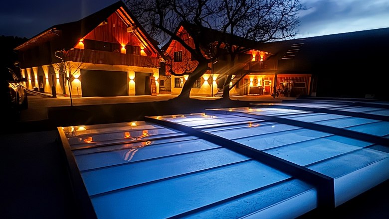 Nachtansicht eines beleuchteten Gebäudes mit Baum und überdachtem Bereich im Vordergrund.