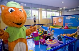 Kinder spielen in einem Indoor-Spielbereich mit einem großen orangefarbenen Maskottchen.