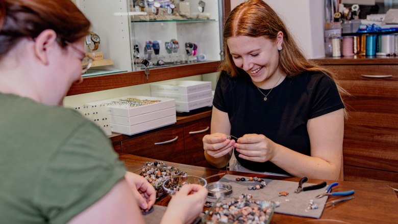 Zwei Frauen fertigen Schmuck aus Granitsteinen an einem Tisch.
