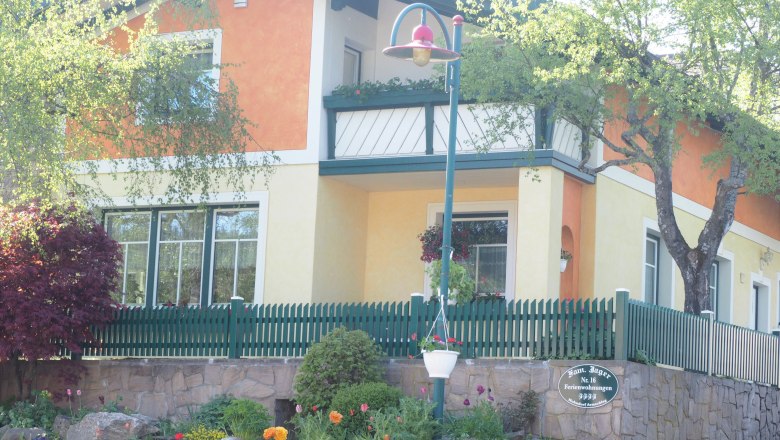 Ein zweist&ouml;ckiges Haus mit orange-gelber Fassade, gr&uuml;nem Zaun und Garten.