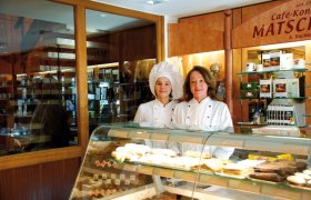 Zwei Frauen in Konditoruniformen stehen hinter einer Theke mit Gebäck in einer Bäckerei.