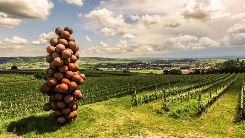 Skulptur aus Kugeln in Form einer Weintraube auf einem Weinberg mit Blick auf eine Landschaft.