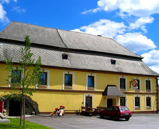 Gelbes Gasthaus mit grauem Dach und rotem Auto davor.