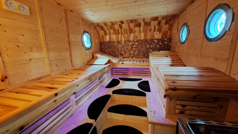 Innenansicht einer Zirbensauna mit Holzbänken und runden Fenstern.