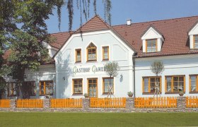 Ein traditionelles Gasthaus mit weißer Fassade und roten Dachziegeln, umgeben von Bäumen und einem Holzzaun.