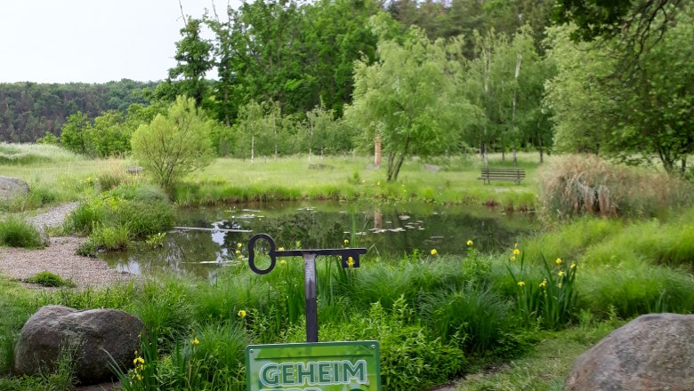 A green pond with trees in the background and a sign saying 'Geheim Tipp' in the foreground.