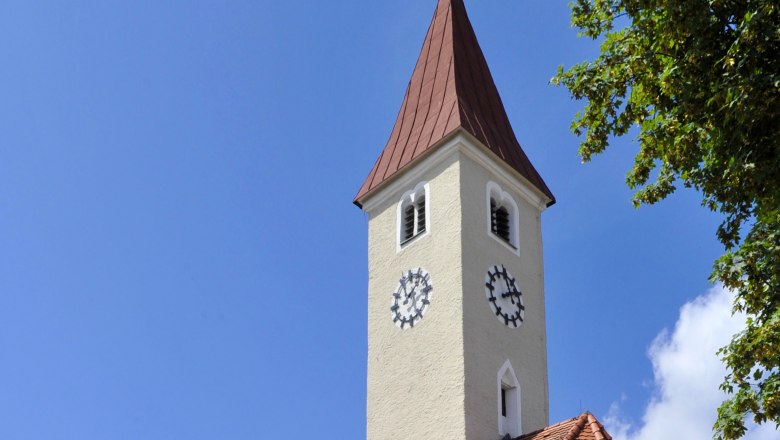 Pfarrkirche Allentsgschwendt mit Turm und Uhr vor blauem Himmel.