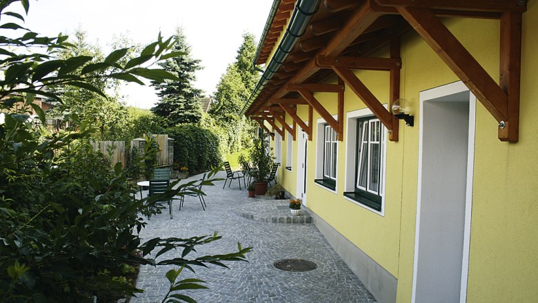 Binder Hof, © Familie Binder Gepflasterter Hof mit gelbem Gebäude und Gartenmöbeln.