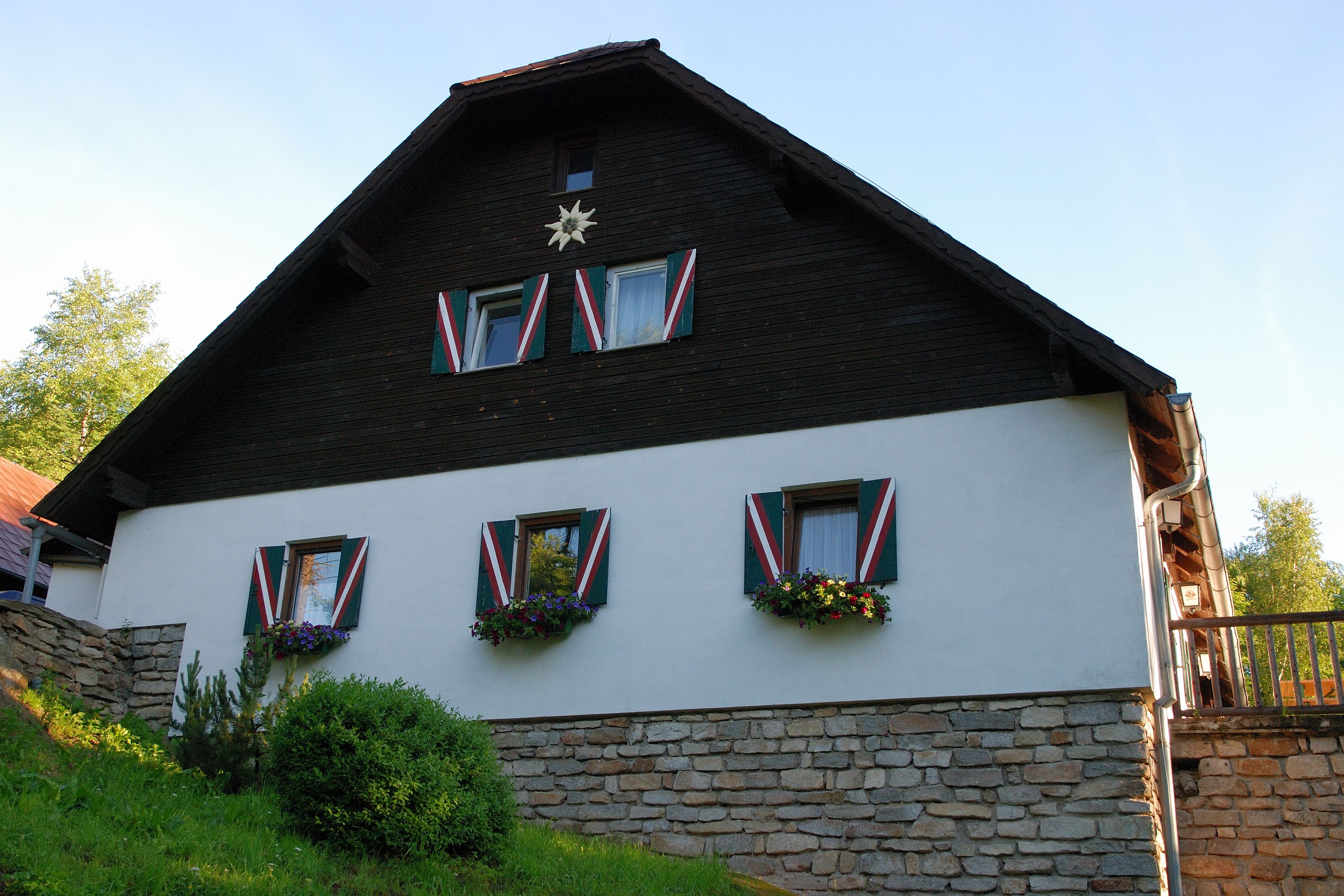 Ein traditionelles Haus mit Holzverkleidung und bunten Fensterläden, umgeben von grüner Vegetation.