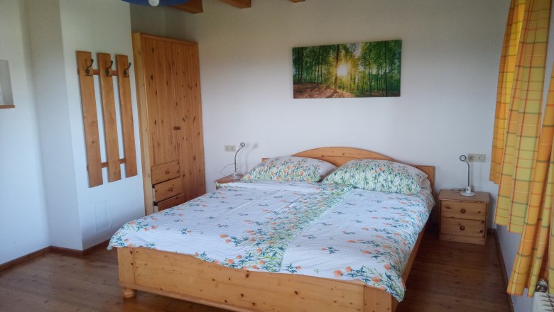 Schlafzimmer mit Holzbett, Nachttischen, Kleiderschrank und Wandbild eines Waldes.