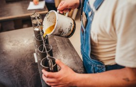 Person gießt flüssiges Wachs in Kerzenformen.