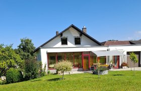 Ein weißes Haus mit rotem Rahmen und Garten vor blauem Himmel.
