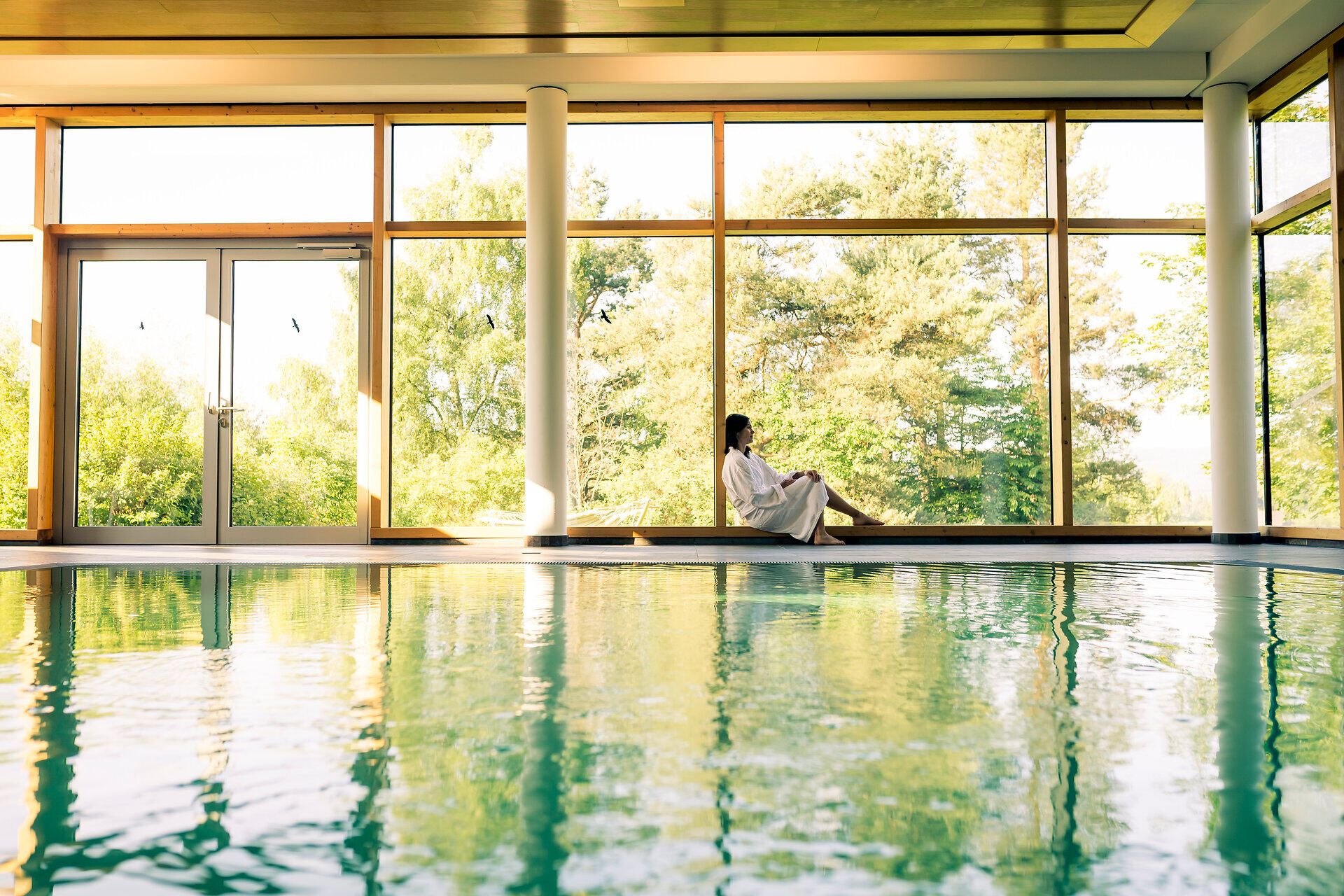 In einem lichtdurchfluteten Wellnessbereich entspannen Gäste in einem ruhigen Ambiente. Die sanften Wellen des Wassers spiegeln die umgebende Natur wider und laden zum Verweilen ein. Hier wird Gesundheit und Wohlbefinden in harmonischer Umgebung großgeschrieben.