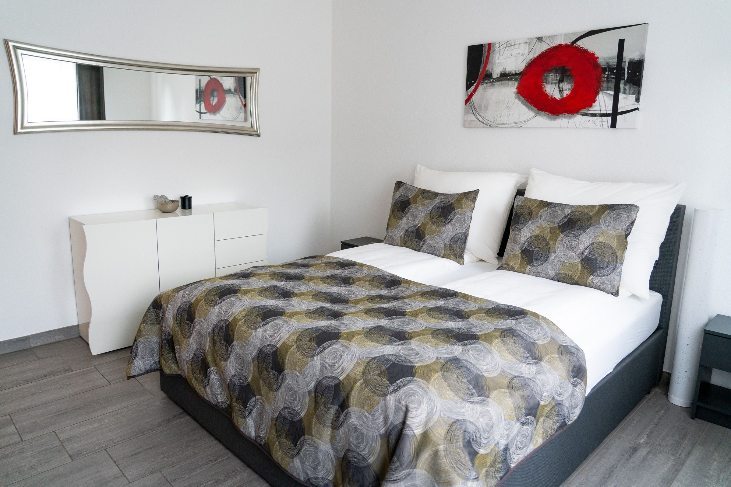 Modernes Schlafzimmer mit Doppelbett, abstraktem Kunstwerk und Spiegel.
