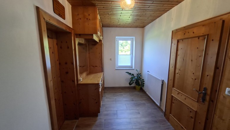 Ein schmaler Flur mit Holzmöbeln, einer Pflanze und einem Fenster mit Blick nach draußen.