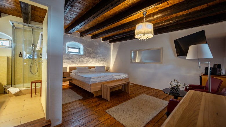 Gemütliches Zimmer mit Holzboden, Doppelbett, Dusche und moderner Einrichtung.