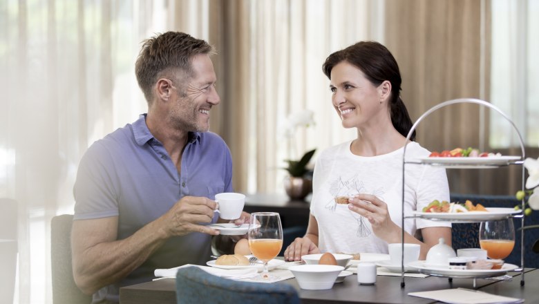 A smiling couple having breakfast at a table with coffee and orange juice.