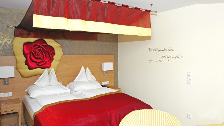 Cozy hotel room with red canopy and rose motif on the wall.