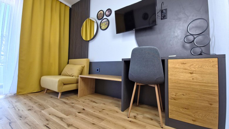 Modern furnished room with yellow armchair, wooden floor, desk and wall decorations.