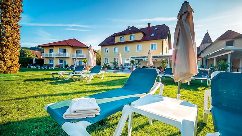 Liegestühle auf einer Wiese vor einem gelben Hotelgebäude bei Sonnenschein.