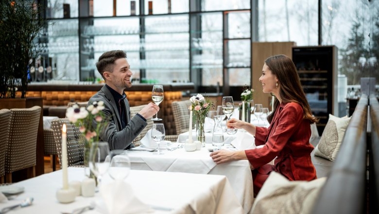 Ein Paar sitzt in einem eleganten Restaurant und stößt mit Weißwein an.