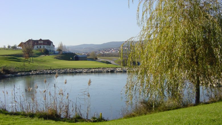 Golf course with pond, trees and a building in the background.