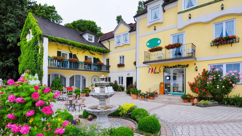 Gelbes Hotelgebäude mit Blumenschmuck und Springbrunnen im Vordergrund.