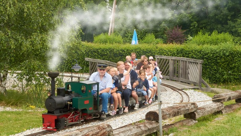 Eine Miniatureisenbahn mit Passagieren fährt durch einen Park.