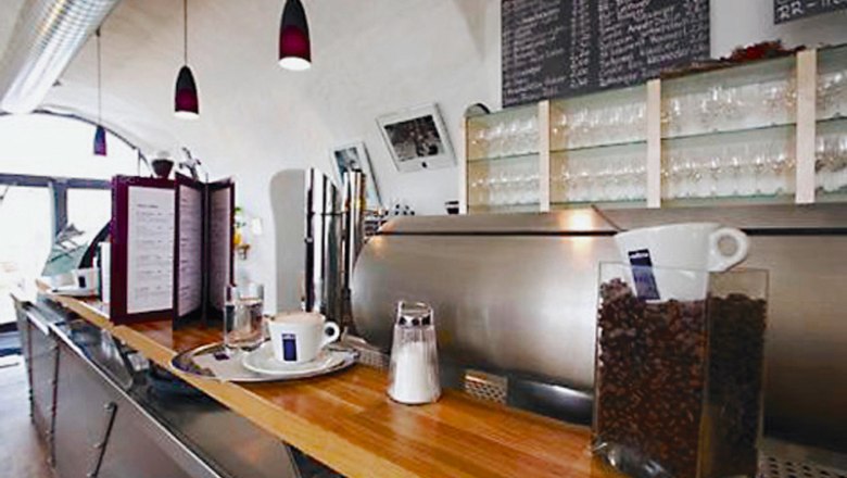 Innenansicht eines Cafés mit Theke, Kaffeemaschine und Gläsern.