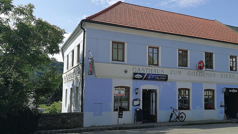 Ein zweistöckiges Gebäude mit der Aufschrift 'Gasthaus zum Goldenen Stern' und einem Fahrrad davor.