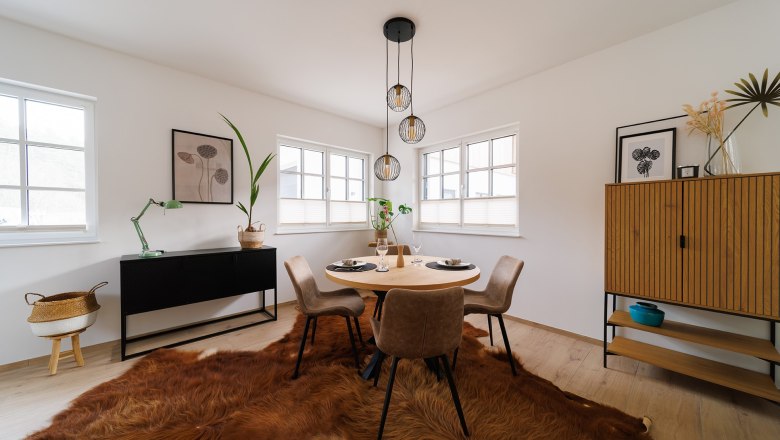 Modernes Esszimmer mit rundem Tisch, vier Stühlen, Fellteppich und minimalistischer Dekoration.