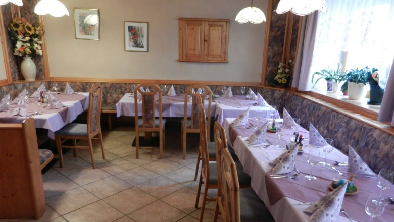 Gemütlicher Gastraum mit gedeckten Tischen und Holzstühlen.