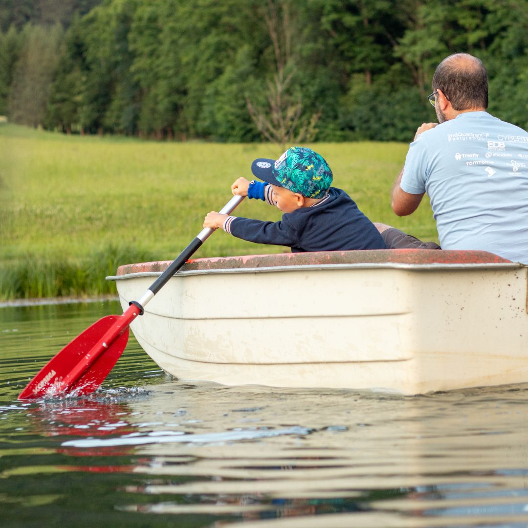 Ein Kind und ein Erwachsener rudern in einem kleinen Boot auf einem Teich.