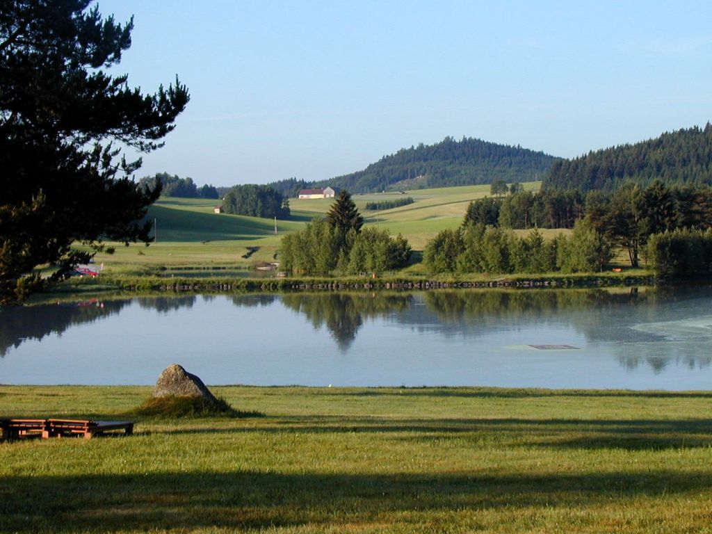Ein ruhiger See mit umliegenden Wiesen und Wäldern in einer ländlichen Landschaft.
