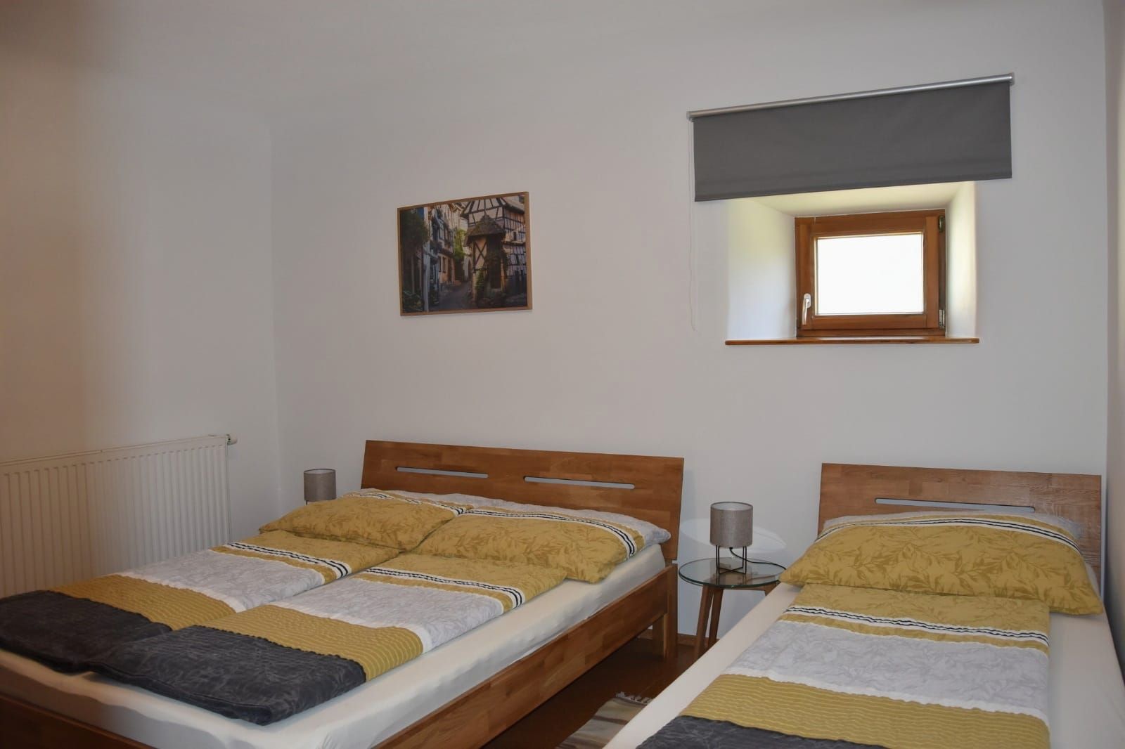 Schlafzimmer mit einem Doppel- und einem Einzelbetten, Nachttisch, Fenster mit Verdunkelungsrolllo.
