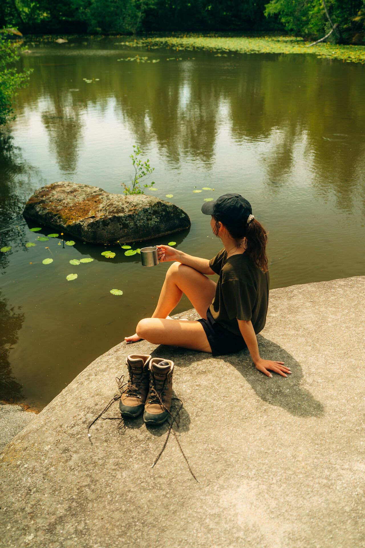 Frau sitzt auf einem Stein in der Blockheide, umgeben von Wald und Wasser