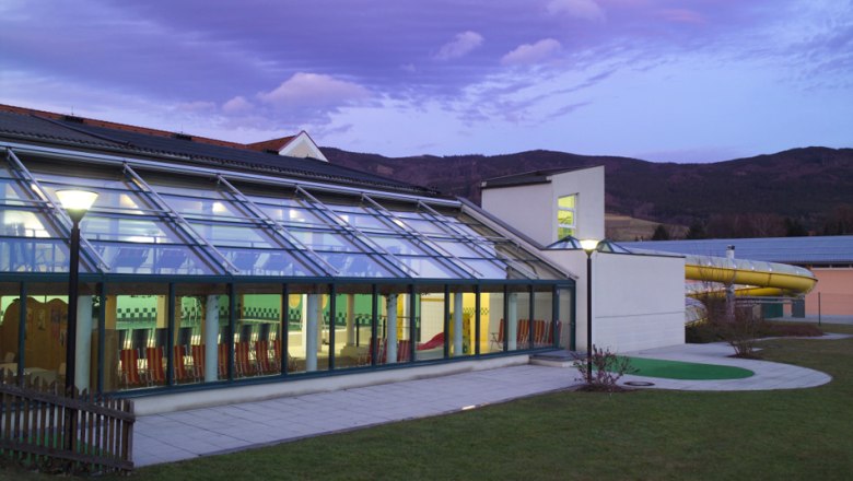 Außenansicht des Hallenbads Yspertal bei Dämmerung mit Glasfassade und Rutsche.