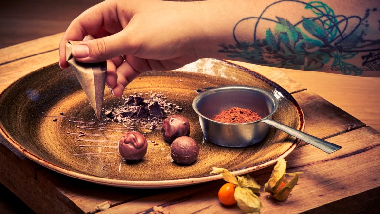 Close-up of a hand with a tattoo decorating chocolate on a plate.