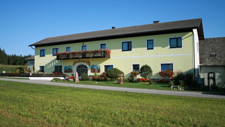 Ein gelbes Bauernhaus mit Blumen und grünem Rasen im Vordergrund.