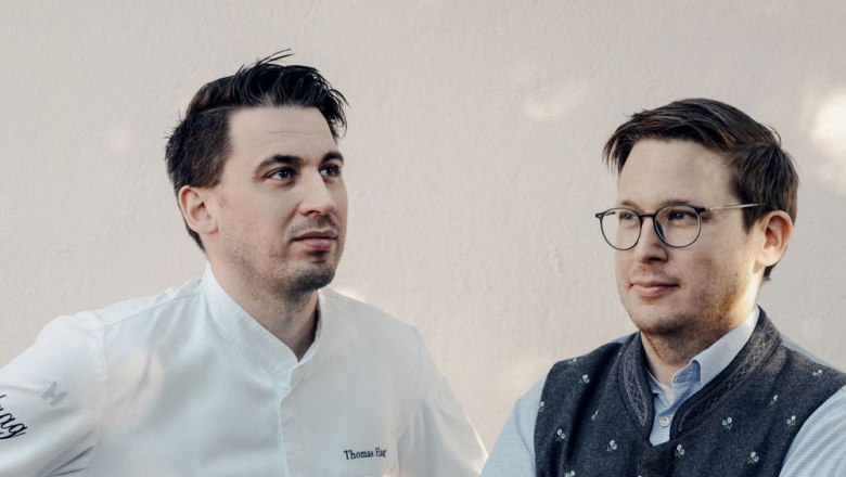 Two men are standing next to each other, one wearing a chef's jacket, the other a traditional vest.