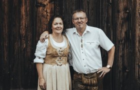 Ein Mann und eine Frau in traditioneller Tracht vor einer Holzwand.