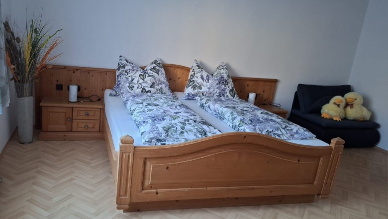 Schlafzimmer mit Doppelbett, Holzm&ouml;beln und zwei Pl&uuml;schenten auf einem Sofa.