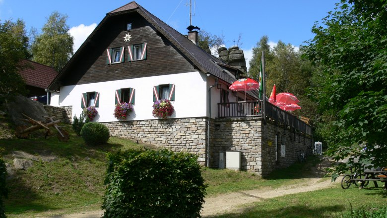 A mountain hut with flowers and parasols on a terrace.