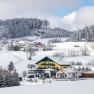 Winter landscape with snow-covered Café-Pension Kristall and surrounding houses.