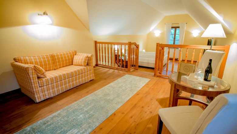 Gemütliches Zimmer mit Sofa, Tisch und Stuhl, Holzboden und Geländer.